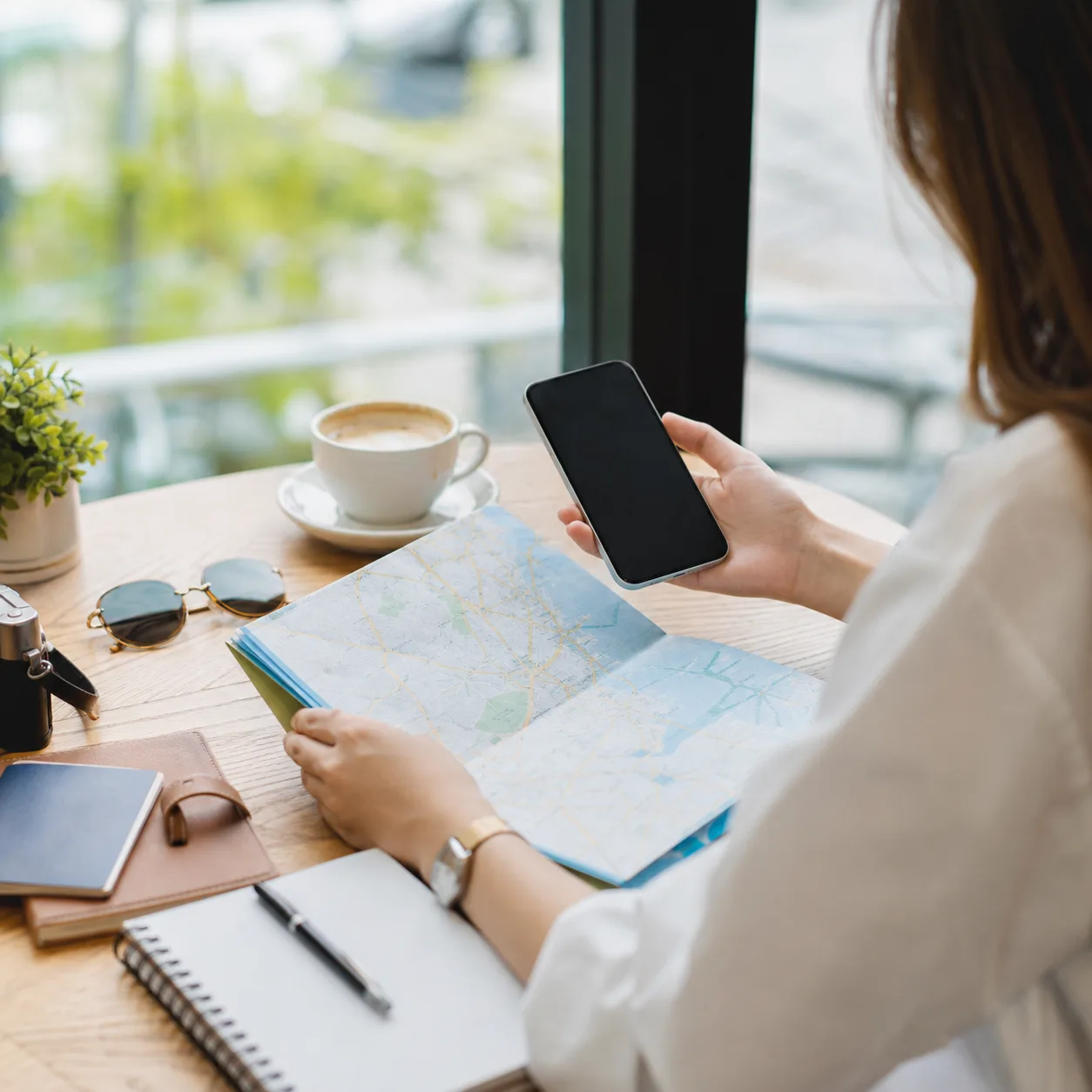 Traveler planning a trip with a map and smartphone at a cafe table